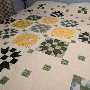 May include: A patchwork quilt with a cream-coloured base and a variety of square patterns. The squares display floral and geometric designs in green, yellow, and black. The quilt is laid out on a bed, highlighting its size and detailed patchwork.