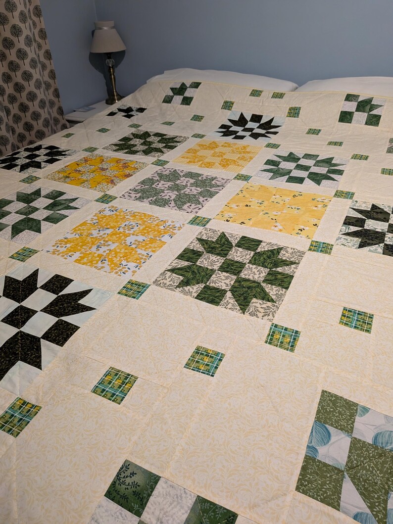 May include: A patchwork quilt with a cream-coloured base and a variety of square patterns. The squares display floral and geometric designs in green, yellow, and black. The quilt is laid out on a bed, highlighting its size and detailed patchwork.