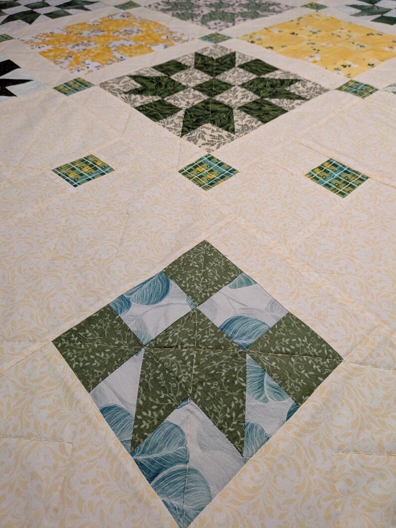 May include: Close-up of a handmade quilt with a diamond pattern. The quilt features various green, yellow, and white floral and geometric designs. The quilt is made of fabric with a soft, quilted texture.