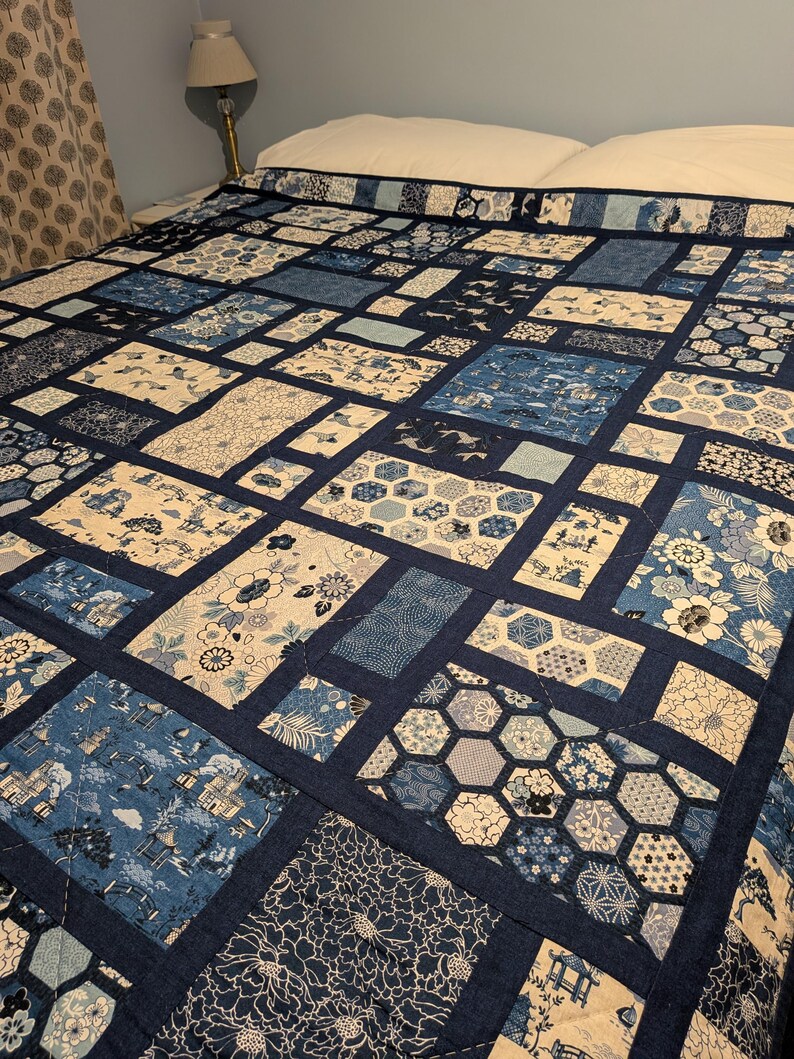 Peut inclure: Une courtepointe faite &agrave; la main avec un motif patchwork dans des tons de bleu et de cr&egrave;me. La courtepointe pr&eacute;sente divers motifs, notamment des motifs floraux, g&eacute;om&eacute;triques et paysagers. La courtepointe est pos&eacute;e sur un lit, mettant en valeur son design et son savoir-faire.