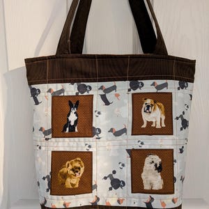 Può includere: Una borsa tote marrone con un motivo a tema cani. La borsa presenta uno sfondo azzurro chiaro con varie razze di cani, tra cui bassotti e barboncini. Quattro pannelli quadrati mostrano immagini ravvicinate di diversi cani. I manici e le finiture sono marrone scuro.
