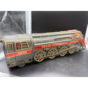 May include: Vintage toy train in gray, red, and gold. The train is labeled "Trans-Continental Express" and has the number "6601" on the side. The train features a red and gold eagle emblem.
