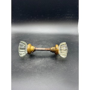 May include: Antique glass door knob with brass hardware. The clear glass knobs have a ribbed design and are attached to a brass base. The connecting rod is a dark brown color. A vintage home decor item.