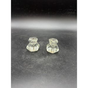 May include: Two clear, faceted glass knobs with a hexagonal top and a rounded base. The knobs are likely for a cabinet or drawer and are displayed against a dark background.