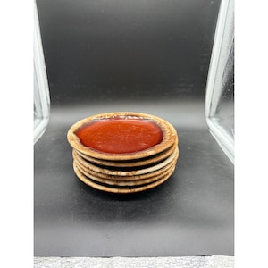 May include: A stack of six small, oval-shaped ceramic plates. Each plate has a dark reddish-brown center and a lighter brown, textured rim. The plates are stacked neatly, showcasing their unique design.