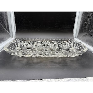 May include: A rectangular clear glass serving tray featuring a pressed starburst pattern across the base and sides. The tray has a scalloped, serrated edge and a faceted surface design that reflects light, creating a textured appearance throughout.