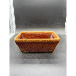May include: A rectangular ceramic bowl featuring a deep brown glaze with a textured, dimpled surface on the exterior sides. The rim is a lighter tan color, and the base displays a subtle vertical ribbed pattern, creating a distinct contrast.