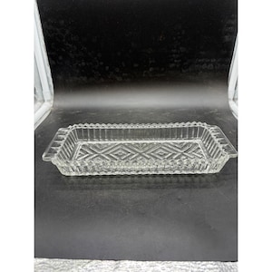 May include: A rectangular clear glass tray featuring a geometric diamond pattern on the base and a serrated, notched rim. The sides of the tray are vertically ribbed, and the piece includes two integrated handles on the short ends.