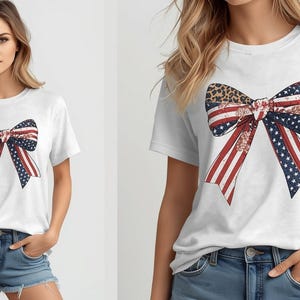 May include: White t-shirt with a patriotic bow design. The bow combines the American flag with red and white stripes, blue stars, and a leopard print centre. The shirt is worn with denim shorts.