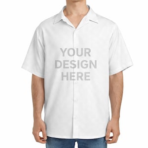May include: A short-sleeved white button-down shirt with a classic collar. The front of the shirt features the grey text "YOUR DESIGN HERE" centred on the chest. The garment is worn over blue denim jeans, showcasing a clean and simple design.