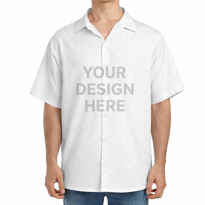 May include: A short-sleeved white button-down shirt with a classic collar. The front of the shirt features the grey text "YOUR DESIGN HERE" centred on the chest. The garment is worn over blue denim jeans, showcasing a clean and simple design.