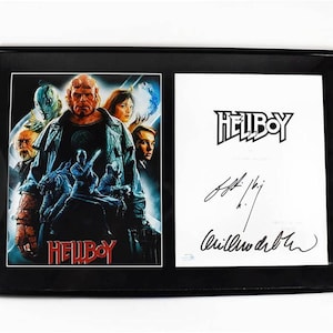 May include: Framed Hellboy movie poster and signed artwork. The poster features a group of characters with the title "Hellboy" in red. The signed artwork includes the "Hellboy" logo and signatures in black ink.
