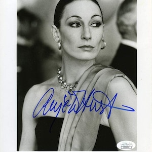Puede incluir: Fotografía en blanco y negro de Anjelica Huston, con un vestido negro y un collar plateado. La imagen está firmada con tinta azul. El texto en la foto dice "PRIZZI'S HONOR".