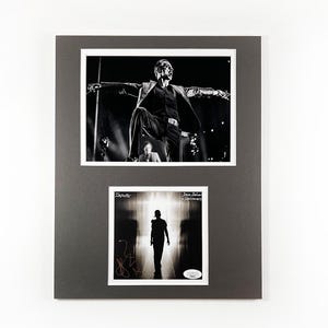 May include: Framed black and white photographs. The top image shows a man in a suit on a stage with arms outstretched. The bottom image is a silhouette of a man walking towards light, with text and a signature.