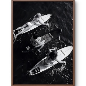 Può includere: Stampa incorniciata in bianco e nero con tre tavole da surf nell'oceano. Ogni tavola ha la scritta "CHANEL". L'immagine mostra tre persone sulle tavole da surf.