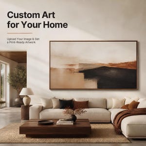 Op de afbeelding: Een groot rechthoekig ingelijst abstract schilderij met beige, bruine en zwarte horizontale kleurvlakken hangt boven een crèmekleurige hoekbank. De tekst op de muur luidt: Custom Art for Your Home. Upload Your Image & Get a Print-Ready Artwork.