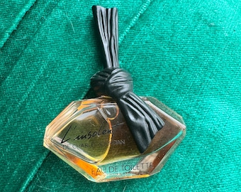 May include: A small, clear glass bottle of perfume with a black ribbon tied around the neck. The bottle is shaped like a diamond and has the text "L'insolent de Charles Jourdan" and "Eau de Toilette" printed on it.
