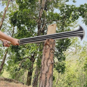 May include: A large, silver-colored sword with a black, curved blade and a ridged handle. The sword is held in front of a tree stump, with a forest background.