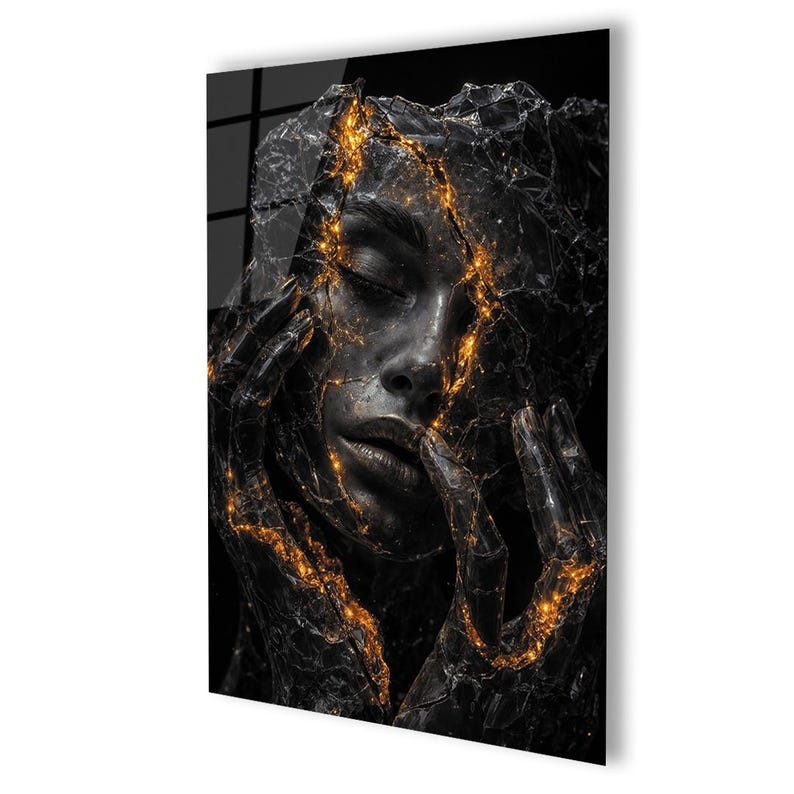 May include: A black and gold abstract art print featuring a woman's face. The face is partially obscured by a cracked, textured surface with glowing gold accents. The woman's hands are near her face, adding to the artistic composition.