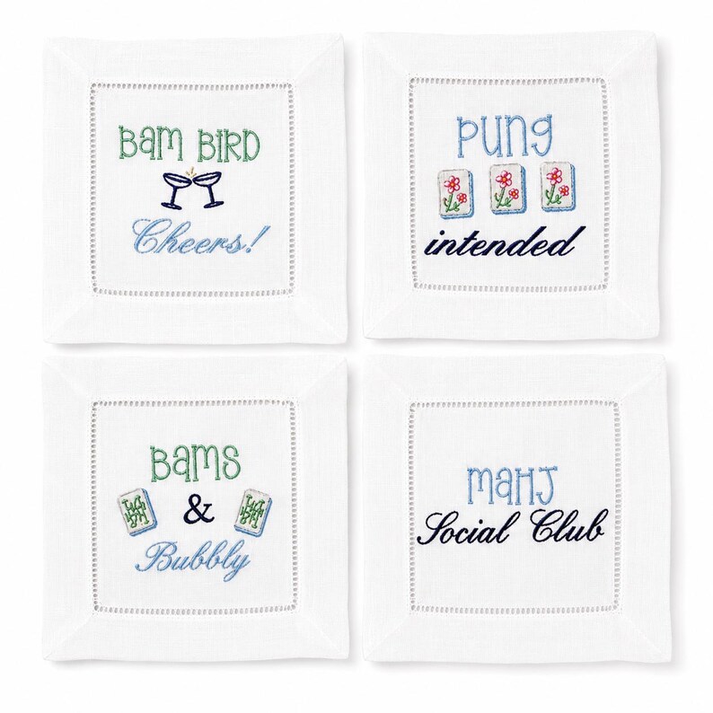 May include: A set of four square white linen coasters with hemstitched borders. Each features colorful embroidery: 'BAM BIRD Cheers!', 'PUNG intended' with three mahjong tiles, 'BAMS & Bubbly' with two mahjong tiles, and 'MAHJ Social Club' in blue and black.