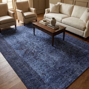 May include: A large, rectangular blue area rug with a distressed pattern. The rug is placed in a living room setting, with a sofa, chairs, and a coffee table. The rug's dimensions are not visible.