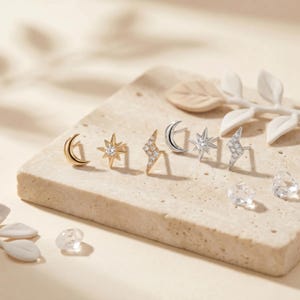 May include: A collection of six stud earrings featuring celestial and weather motifs. The set includes gold-toned crescent moon, starburst, and lightning bolt shapes, alongside silver-toned versions, each accented with small clear stones.