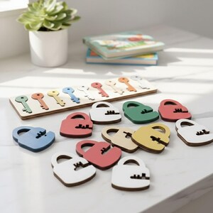 K&ouml;nnte beinhalten: Ein Holzschl&uuml;ssel- und Schloss-Zuordnungsspiel. Das Puzzle besteht aus einer Holzbasis mit schl&uuml;sself&ouml;rmigen Aussparungen und einer Reihe farbiger Schl&ouml;sser. Die Schl&ouml;sser sind in verschiedenen Farben erh&auml;ltlich, darunter Blau, Rot, Gr&uuml;n und Gelb.