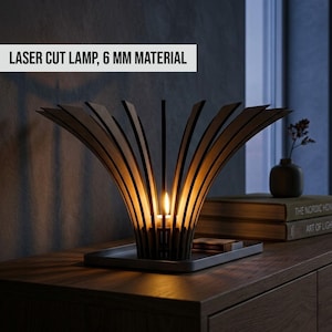 May include: A laser-cut wooden lamp with a unique, fan-like design. The lamp features a central candle holder, and the text "LASER CUT LAMP, 6 MM MATERIAL" is displayed on the top. The lamp sits on a gray tray.