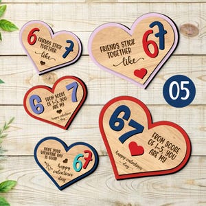 Peut inclure: Plusieurs décorations en forme de cœur en bois avec des messages et des chiffres. Les cœurs affichent des phrases telles que « Les amis restent ensemble comme » et « De la note de 1 à 5, tu es à moi ». Chaque cœur a un code couleur unique, rouge, bleu et rose.