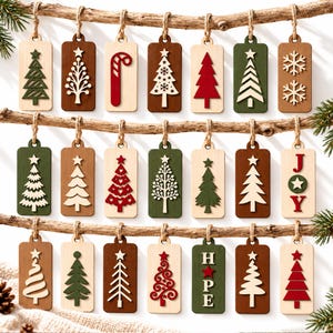 Könnte beinhalten: Eine Sammlung von einundzwanzig rechteckigen Geschenkanhängern aus Holz, die an drei horizontalen Zweigen hängen. Die Anhänger zeigen lasergeschnittene Motive wie verschiedene Weihnachtsbäume, Schneeflocken, eine Zuckerstange sowie die Wörter JOY und HOPE.