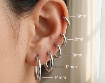 Op de afbeelding: Een set van vijf gepolijste zilverkleurige oorringen in verschillende maten, gelabeld met afmetingen van 6mm, 8mm, 10mm, 12mm en 14mm. De ringen zijn in een verticale rij langs het oor geplaatst en hebben een glad, afgerond metaalontwerp.