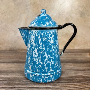 May include: A vintage blue and white enamelware coffee pot with a black handle and spout. The pot has a speckled pattern and a lid with a small knob. The coffee pot is a classic kitchenware item.