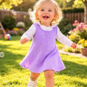 Può includere: Una bambina con i capelli biondi e gli occhi azzurri, indossa una camicia bianca a maniche lunghe e un vestito di lana lilla, corre su un prato. La bambina sorride e indossa scarpe da ginnastica rosa e bianche. Lo sfondo include alberi, fiori e bolle di sapone.