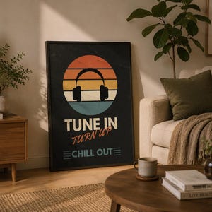 May include: A rectangular framed wall art print featuring a black background with a central circular graphic of a sunset in orange, yellow, and blue stripes. A black silhouette of headphones is centered, with the text TUNE IN TURN UP CHILL OUT.