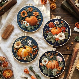 Puede incluir: Cuatro aros de bordado redondos con diseños detallados de calabazas y flores. Cada aro tiene un fondo azul marino con una calabaza naranja y varias flores en tonos naranja, blanco y verde. Los aros se exhiben sobre una tela blanca y una superficie de madera.