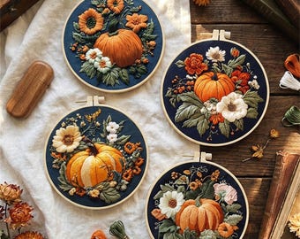 Puede incluir: Cuatro aros de bordado redondos con diseños detallados de calabazas y flores. Cada aro tiene un fondo azul marino con una calabaza naranja y varias flores en tonos naranja, blanco y verde. Los aros se exhiben sobre una tela blanca y una superficie de madera.