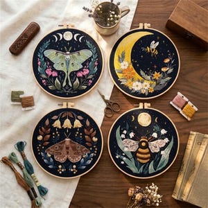 May include: Four circular embroidery hoops featuring nature-themed designs on dark fabric. The designs include a green moth with moon phases, a yellow crescent moon with a bee, a brown moth with hanging flowers, and a bee with white flowers.
