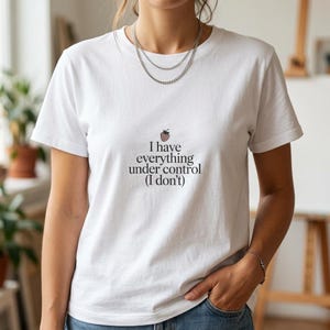 May include: White t-shirt featuring the text "I have everything under control (I don't)" and a strawberry illustration. The top has a crew neck and short sleeves.