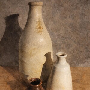 May include: Still life composition featuring three ceramic vases in varying sizes and shapes. The largest vase is tall and slender, while the other two are smaller and more rounded. The vases are in neutral tones, with a textured surface.