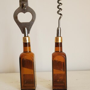 May include: Two vintage bottle openers. One is a bottle opener and the other is a corkscrew. Both have brown glass bottle bases with gold-colored bands. The bottle opener is made of silver-colored metal.