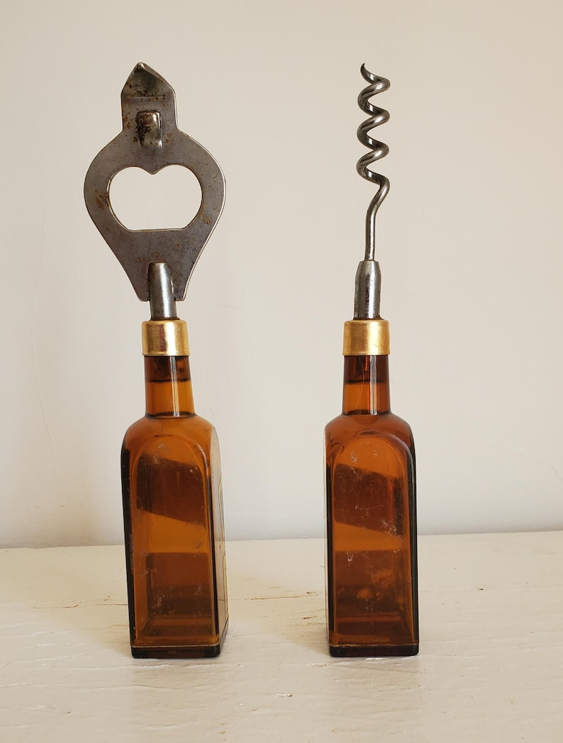 May include: Two vintage bottle openers. One is a bottle opener and the other is a corkscrew. Both have brown glass bottle bases with gold-colored bands. The bottle opener is made of silver-colored metal.