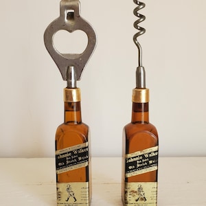 May include: Two vintage bottle openers, one a bottle cap opener and the other a corkscrew, each mounted on a miniature brown glass bottle. The bottles have labels that read "Johnnie Walker Old Scotch Whisky".