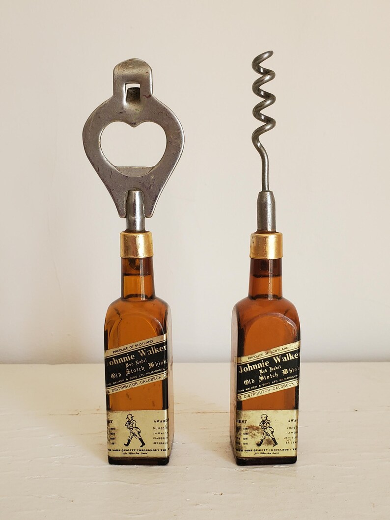 May include: Two vintage bottle openers, one a bottle cap opener and the other a corkscrew, each mounted on a miniature brown glass bottle. The bottles have labels that read "Johnnie Walker Old Scotch Whisky".