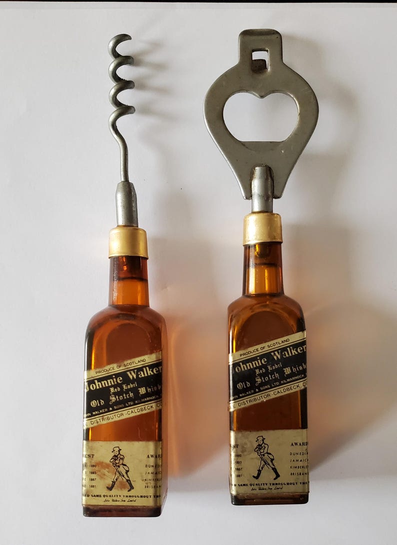 May include: Two vintage Johnnie Walker Old Scotch Whisky bottle-shaped bar tools. One is a corkscrew, the other a bottle opener. Both have amber-colored glass bodies, gold-colored metal accents, and labels with text and a walking figure.