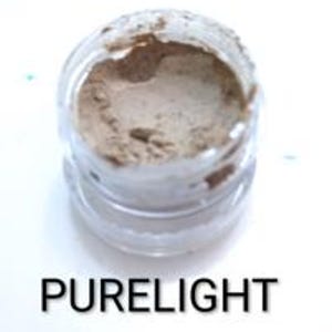Pode incluir: Um pequeno frasco de vidro transparente cheio de pó castanho claro. O frasco está aberto, revelando o conteúdo, contra um fundo branco brilhante. O texto "PURELIGHT" é exibido em preto abaixo.