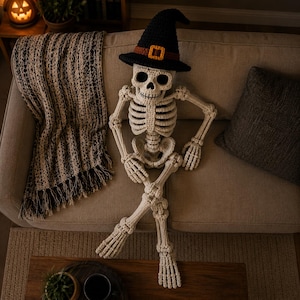 May include: A crocheted off-white skeleton figure wearing a black pointed hat with a brown band and a yellow buckle. The skeleton has a detailed rib cage, skull, and articulated limbs, crafted from yarn with visible stitching throughout the structure.