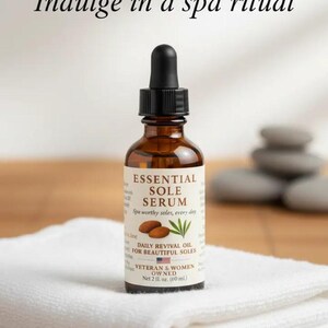Puede incluir: Una botella de vidrio marr&oacute;n de Essential Sole Serum con un cuentagotas negro est&aacute; sobre una toalla blanca. La etiqueta dice "Daily Revival Oil for Beautiful Soles". El texto "Indulge in a spa ritual" est&aacute; en la parte superior.