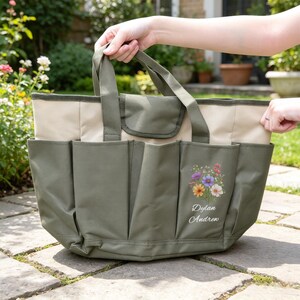 Puede incluir: Una bolsa de jard&iacute;n verde y beige con m&uacute;ltiples bolsillos y asas. La bolsa presenta un dise&ntilde;o floral con los nombres "Dylan Andrew" impresos debajo. La bolsa est&aacute; dise&ntilde;ada para transportar herramientas y suministros de jardiner&iacute;a.