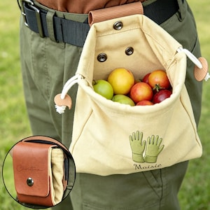 May include: A beige canvas harvest bag, filled with fruit, attached to a belt. The bag has a drawstring closure and wooden toggles. Embroidered on the bag are green gardening gloves and the name "Maisie". A small brown leather pouch is also visible.