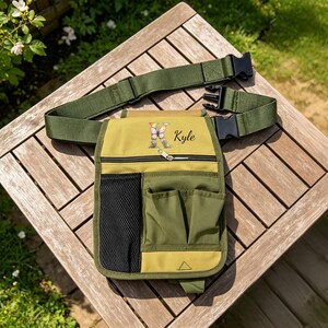 May include: A gardening tool belt with multiple pockets and a belt. The belt is olive green, and the tool belt is olive green and yellow. The tool belt has the name "Kyle" printed on it.